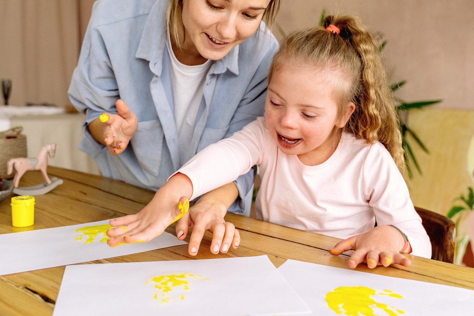 A therapist and a young girl paint with yellow paint at a table